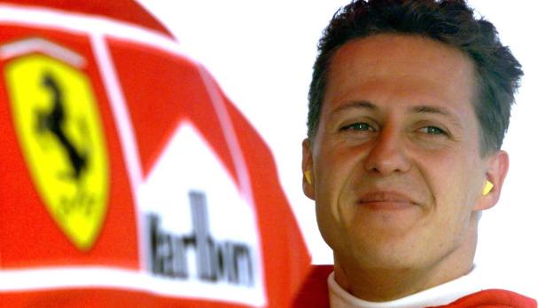 Michael Schumacher mit Ohrstöpseln neben einem Ferrari-Rennwagen.