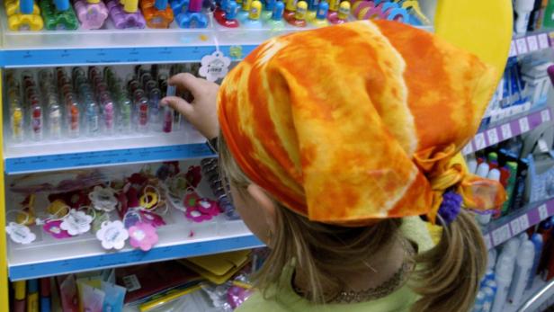 Ein Mädchen mit einem orangefarbenen Kopftuch betrachtet Kosmetikartikel in einem Geschäft.