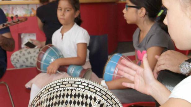 Kinder sitzen im Kreis und spielen auf kleinen Trommeln.