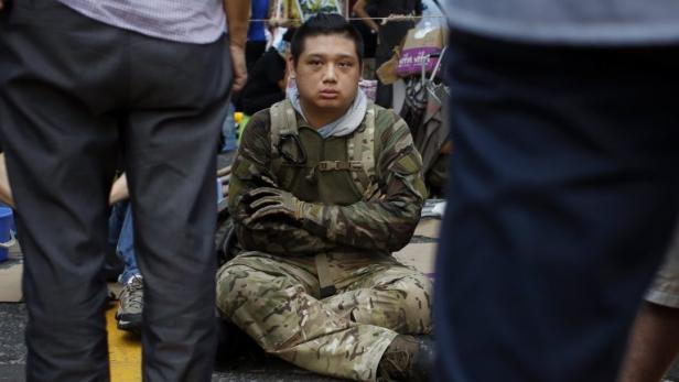 Ein Mann in Tarnkleidung sitzt inmitten einer Menschenmenge auf dem Boden.