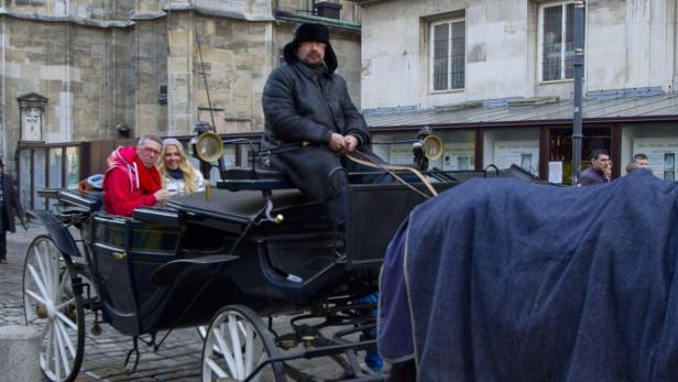 Eine Pferdekutsche mit Fahrgästen und Kutscher in einer Stadt.