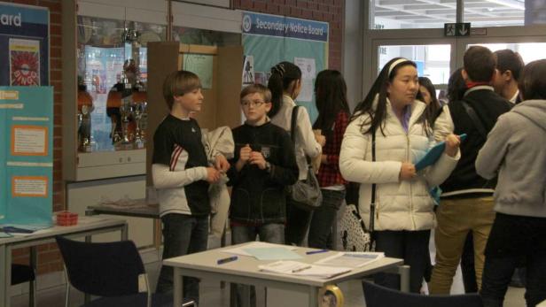 Eine Gruppe von Schülern steht in einem Flur vor einem Schaukasten.