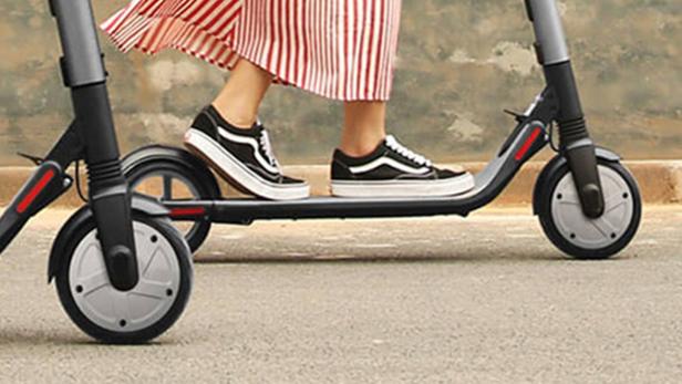 Eine Person mit Vans-Schuhen fährt auf einem Elektroroller.