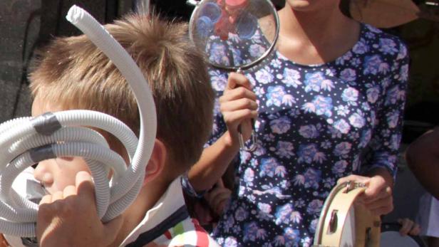 Kinder musizieren mit ungewöhnlichen Instrumenten wie einem Schlauch und einem Sieb.