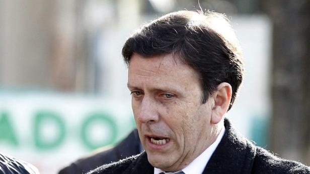 Ein Mann mit dunklen Haaren und einem dunklen Mantel spricht.