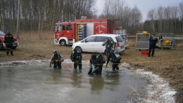Feuerwehrtaucher steigen in einen zugefrorenen See, während andere Einsatzkräfte am Ufer stehen.