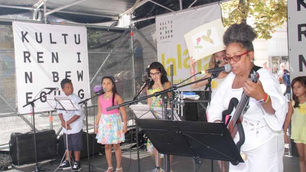 Eine Gruppe von Kindern und eine Frau treten auf einer Bühne auf.