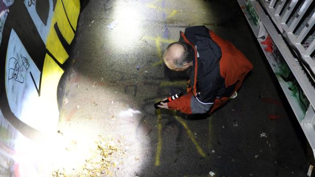Ein Mann untersucht mit einer Taschenlampe Graffiti auf dem Boden.