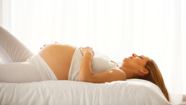 Eine schwangere Frau liegt nachdenklich im Bett.