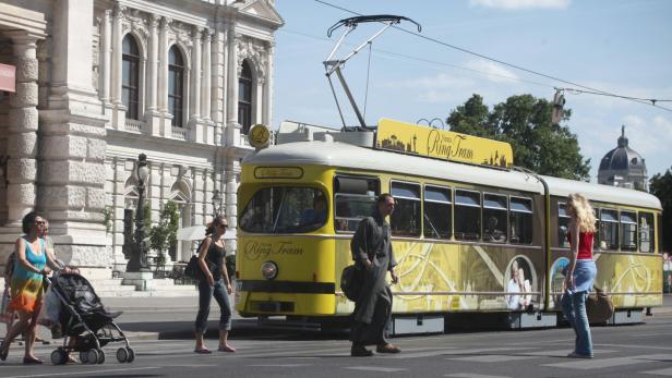 Eine gelbe Ring Tram fährt durch Wien, während Passanten die Straße überqueren.