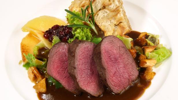 Ein Teller mit gebratenem Hirsch, Semmelknödeln, Preiselbeeren und Pfifferlingen in Soße.