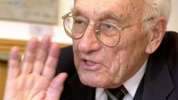 Ein älterer Mann mit Brille gestikuliert mit der Hand.