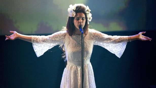 Lana Del Rey singt mit Blumen im Haar auf einer Bühne.