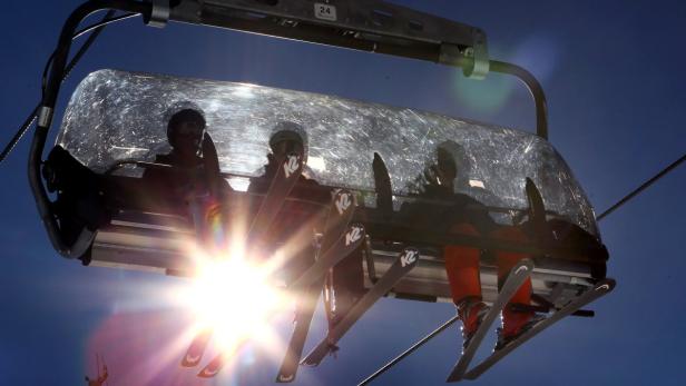 Skifahrer sitzen in einem Sessellift vor blauem Himmel.