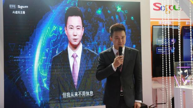 Xinhua news anchor Qiu Hao stands next to an AI virtual news anchor based on him, at a Sogou booth during an expo at the fifth World Internet Conference (WIC) in Wuzhen