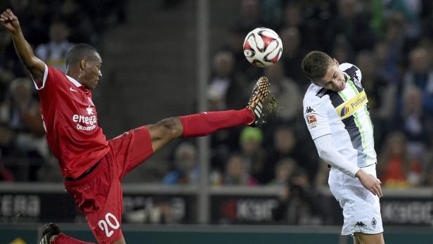 Ein Fußballspieler in Rot schießt den Ball, während ein anderer Spieler in Weiß sich duckt.