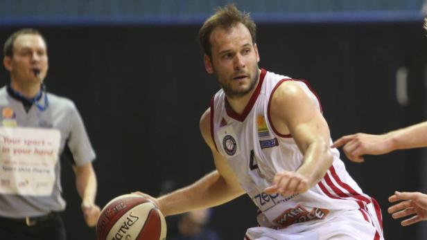 Ein Basketballspieler dribbelt den Ball, während ein Schiedsrichter zusieht.