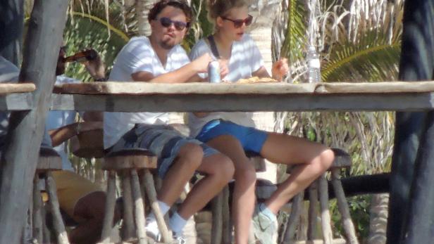 Leonardo DiCaprio und eine Frau sitzen an einem Tisch im Freien und essen Pizza.