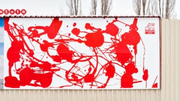 Ein Werbeplakat mit roter Farbspritzer-Kunst an einer Straße.
