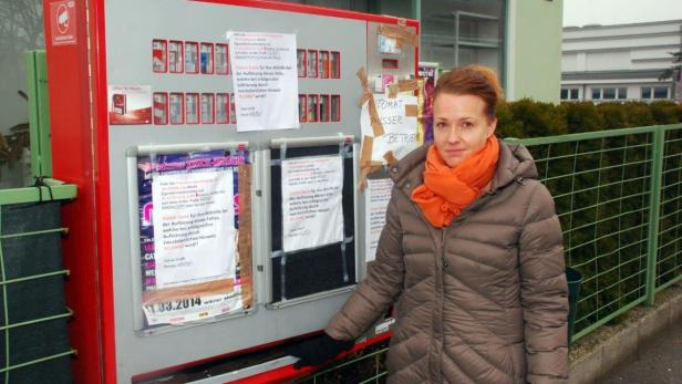 Eine Frau steht vor einem Zigarettenautomaten mit Aushängen.