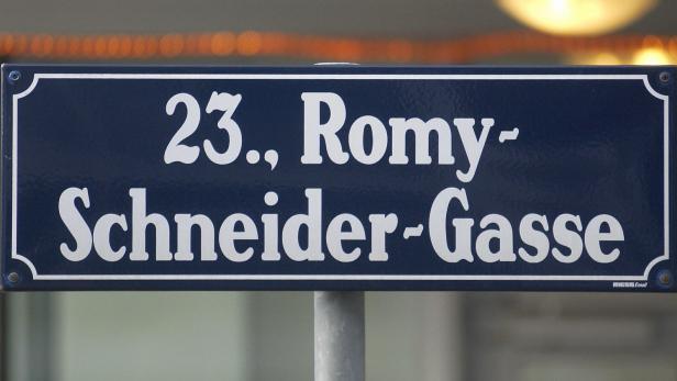 Ein blaues Straßenschild mit weißer Schrift zeigt den Namen „23., Romy-Schneider-Gasse“.