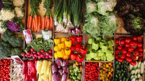 Eine vielfältige Auswahl an frischem Gemüse, darunter Kohl, Karotten, Paprika und Tomaten, in Holzkisten präsentiert.
