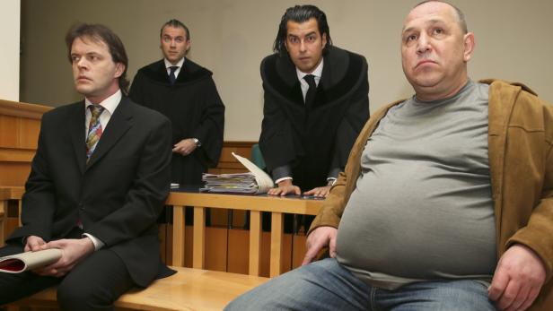 Ein Mann sitzt mit zwei Richtern und einem Anwalt in einem Gerichtssaal.