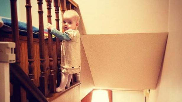 Ein kleines Kind steht an einem Treppengeländer.