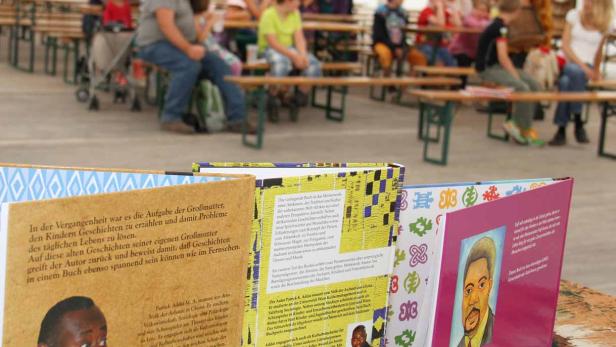 Eine Gruppe von Menschen sitzt auf Bänken hinter einer Auswahl von Büchern des ghanaisch-österreichischen Autors Patrick Addai.