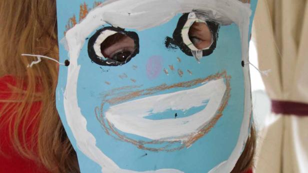 Ein Kind trägt eine selbstgemalte Maske vor dem Gesicht.