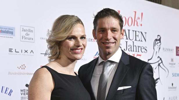 Ein Mann im Anzug und eine Frau in einem schwarzen Kleid posieren auf einem roten Teppich.