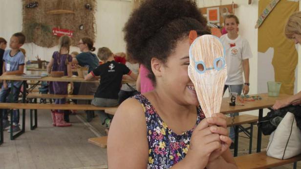 Ein Mädchen hält eine selbstgebastelte Maske vor ihr Gesicht.