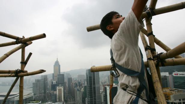 Ein Bauarbeiter auf einem Bambusgerüst mit Blick auf die Skyline von Hongkong.