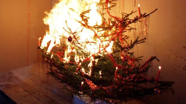 Ein brennender Weihnachtsbaum mit Kerzen und rotem Lametta steht in einem Raum.
