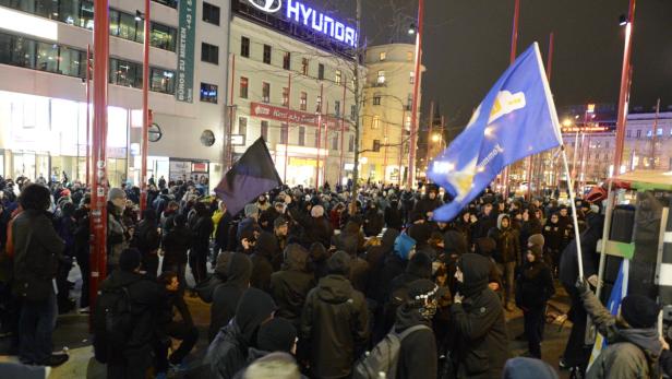 Eine Menschenmenge demonstriert nachts mit Fahnen in einer Stadt.