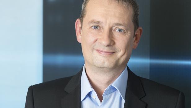 Ein Mann mit Anzug und hellblauem Hemd lächelt in die Kamera.