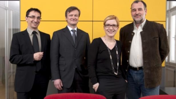 Vier Personen posieren vor einer gelben Wand für ein Gruppenfoto.