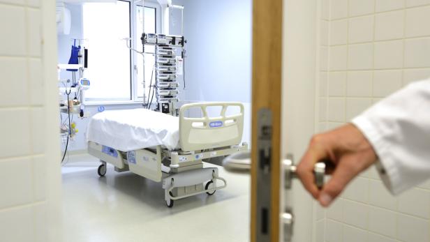 Ein Blick durch eine geöffnete Tür auf ein leeres Patientenzimmer mit einem Krankenbett.