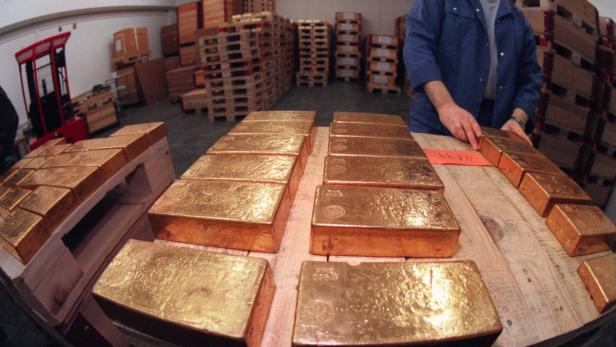 Ein Mann inspiziert Goldbarren, die auf Paletten in einem Lagerhaus gestapelt sind.