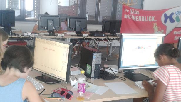Kinder arbeiten an Computern in einem Raum mit einem „KiKu“-Banner.