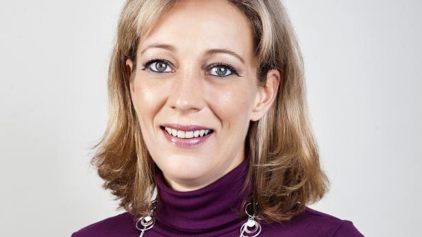 Eine lächelnde Frau mit blonden Haaren und einem lila Rollkragenpullover.