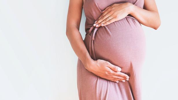 Pregnant woman in dress holds hands on belly on a white background.