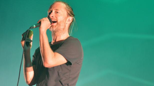 Thom Yorke singt in ein Mikrofon vor einem grünen Hintergrund.