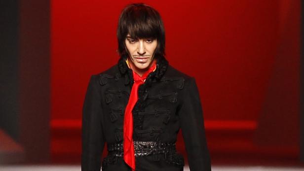 Ein Mann mit dunklen Haaren und roter Krawatte auf einem roten Laufsteg.