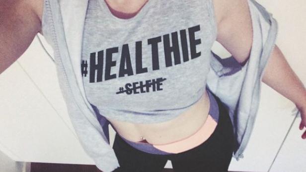 Eine Frau macht ein Selfie in Sportkleidung mit dem Aufdruck „#Healthie #Selfie“.