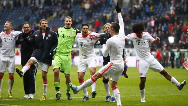Fußballspieler des FC Bayern München feiern auf dem Rasen mit einem Megaphon.
