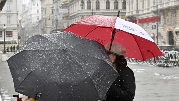 Zwei Personen mit Regenschirmen gehen durch eine verschneite Stadt.