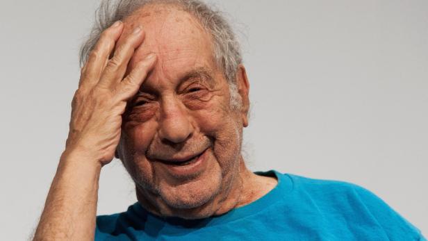 Ein älterer Mann mit einem blauen T-Shirt lächelt und hält seine Hand an die Stirn.