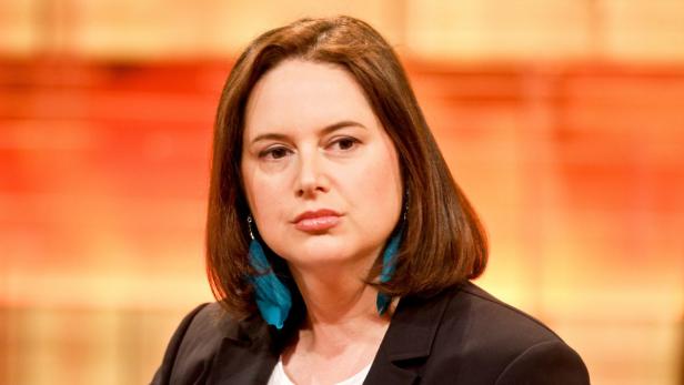 Eine Frau mit braunen Haaren und blaugrünen Ohrringen blickt in die Kamera.