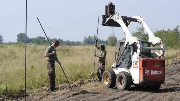 Zwei Arbeiter installieren mit einem Bobcat-Lader einen Zaun in einem Feld.